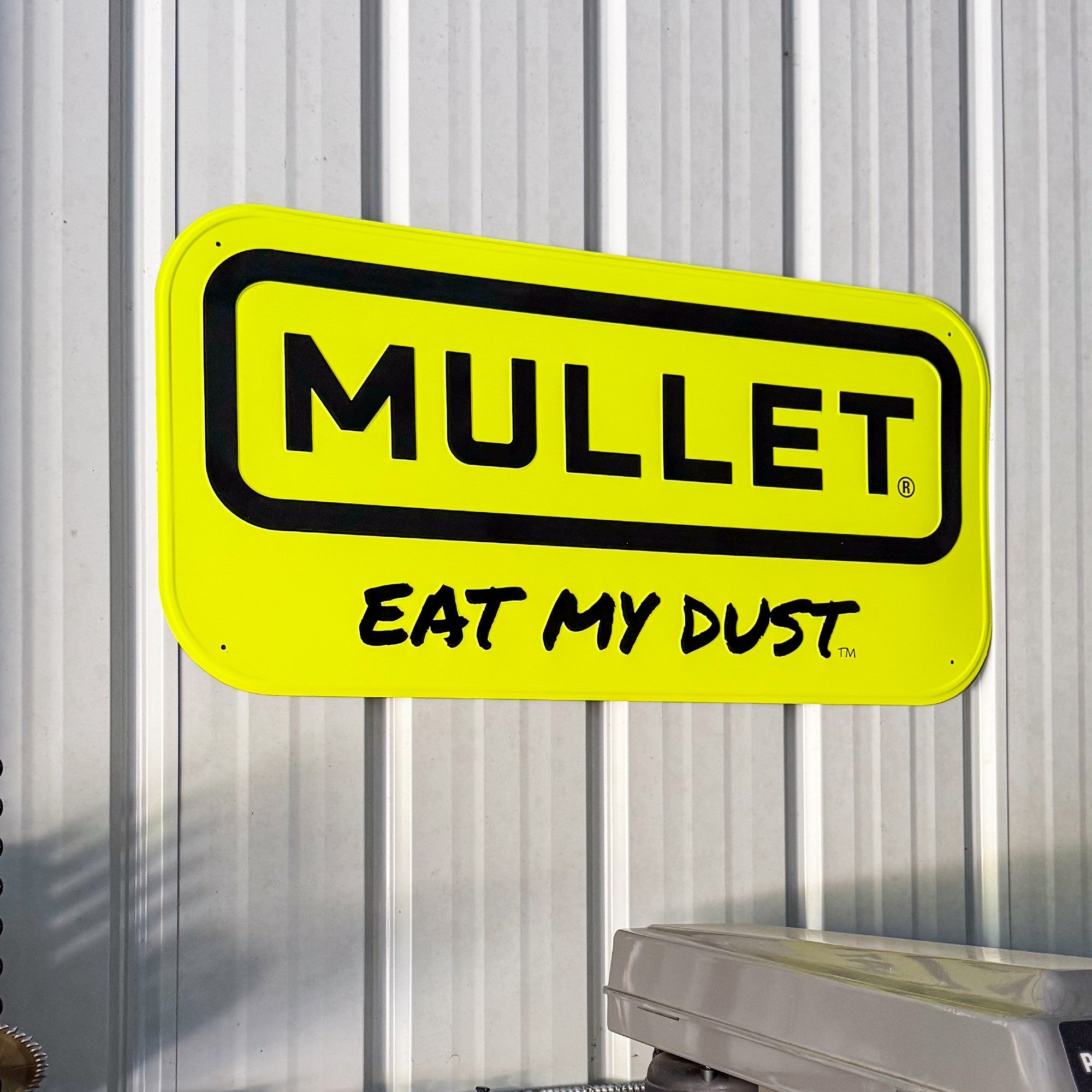 Yellow sign with 'Mullet Eat My Dust' text on a corrugated metal background